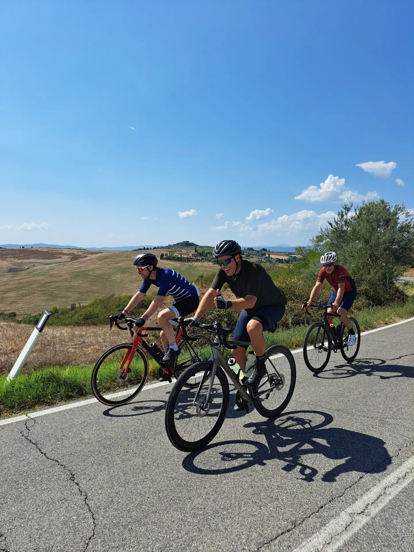 Drie fietsers naast elkaar op een weg door Toscaans heuvelland