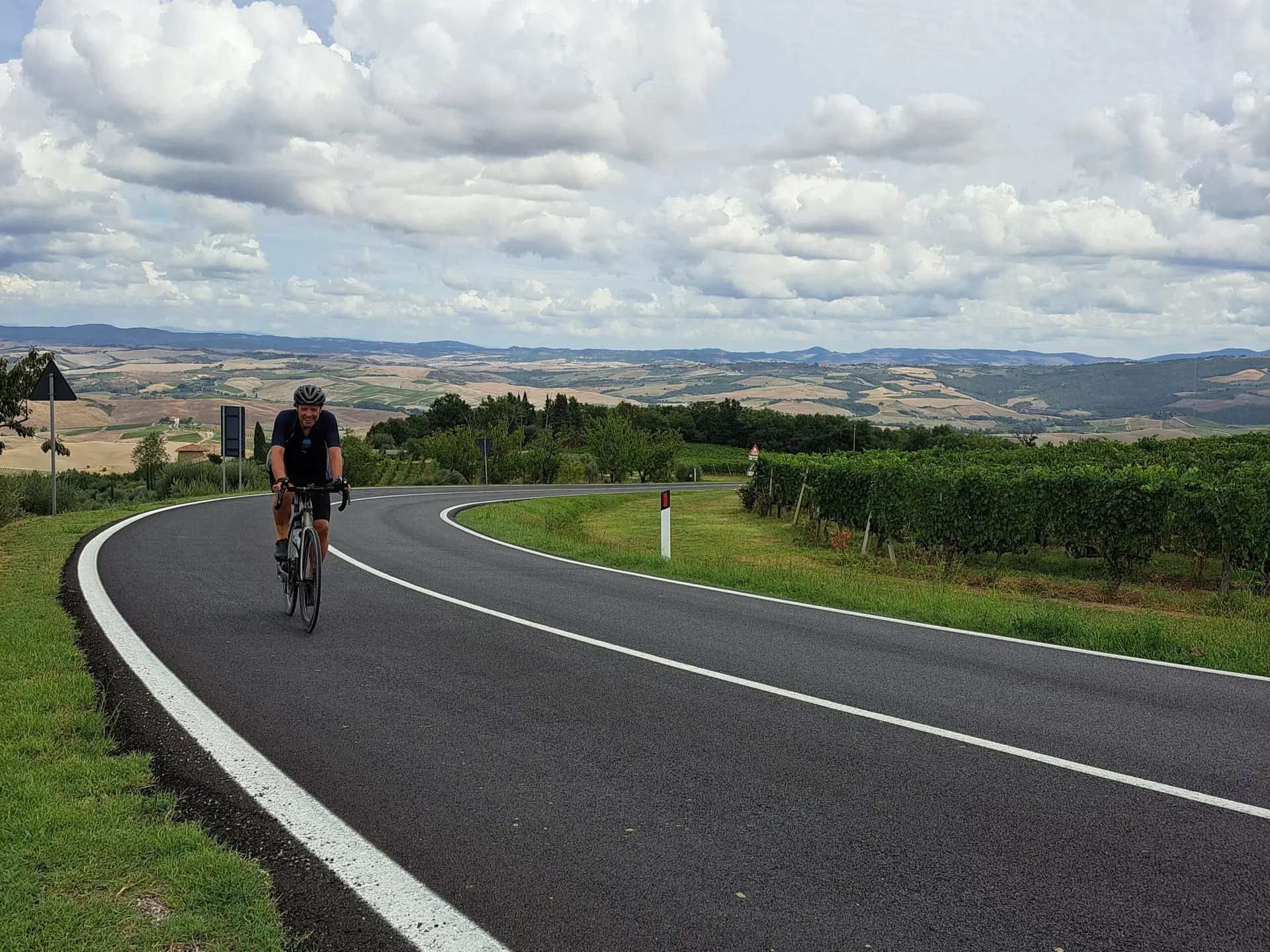 Eenzame fietser op een brede weg langs wijngaarden in Toscane