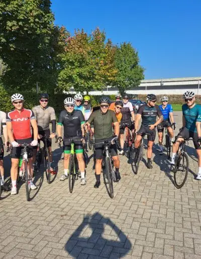 Grote groep fietsers poseert met hun fietsen op een plein in herfstzon