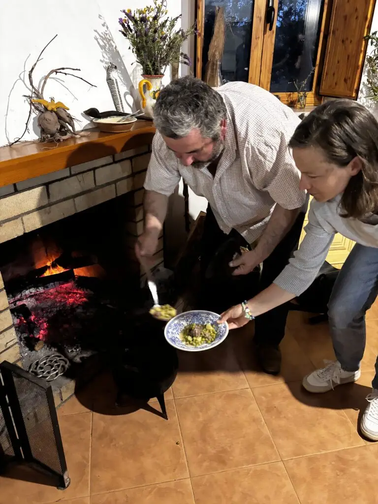 Man en vrouw scheppen eten uit een pan bij het open haardvuur