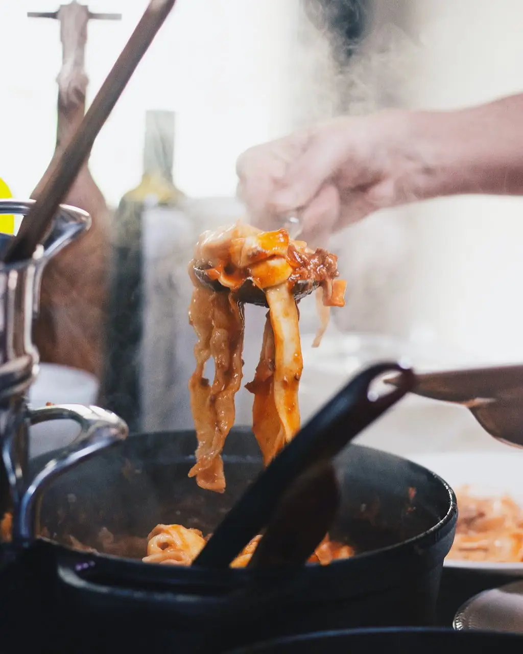 Kok schept dampende pasta met tomatensaus uit een gietijzeren pan