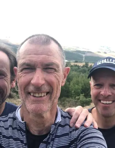 Close-upselfie van drie lachende mannen in een heuvelachtig landschap