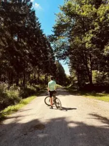 Fietser staat met zijn fiets op een grindweg door dicht naaldbos