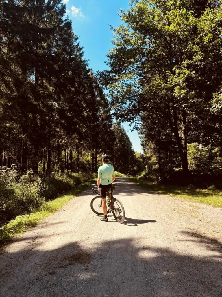 Fietser staat met zijn fiets op een grindweg door dicht naaldbos