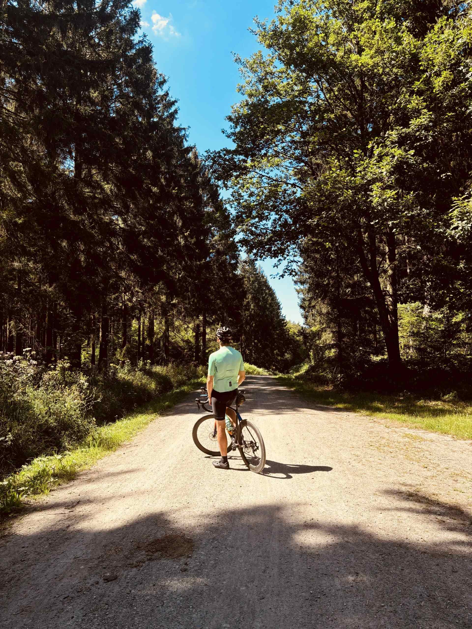 Fietser staat met zijn fiets op een grindweg door dicht naaldbos