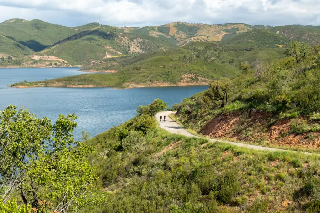 Twee fietsers op een weg langs een stuwmeer in groene Algarve-heuvels