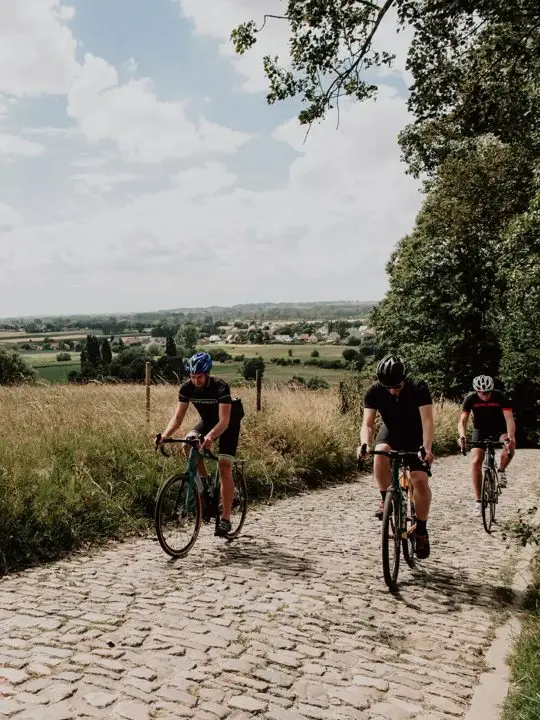 Drie fietsers beklimmen de kasseien van de Koppenberg boven Vlaams akkerland