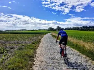 Fietser klimt over de kasseien van de Oude Kwaremont tussen de akkers