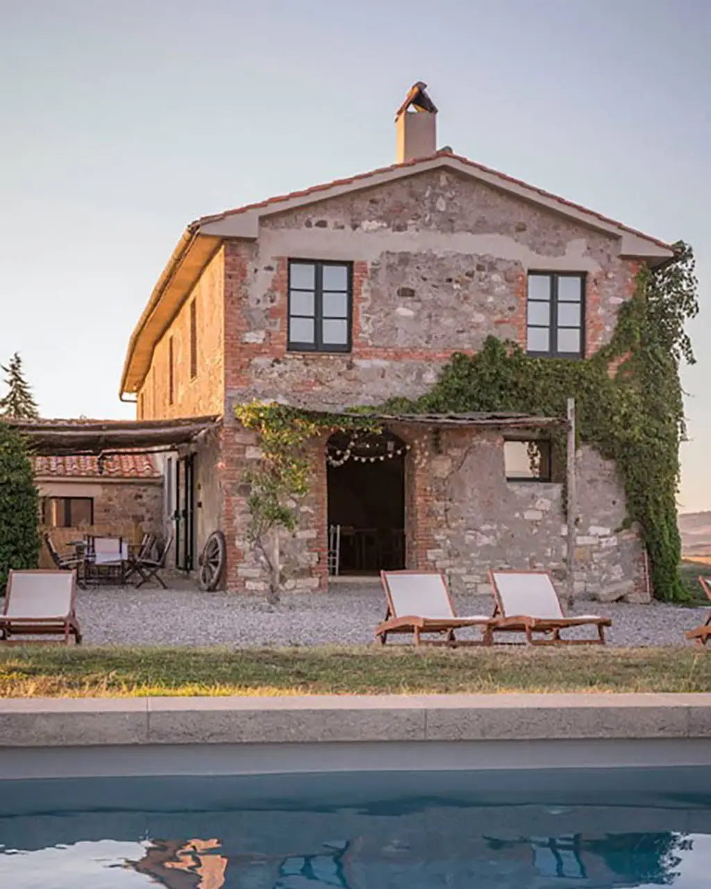 Toscaans stenen landhuis met zwembad en ligstoelen in avondlicht