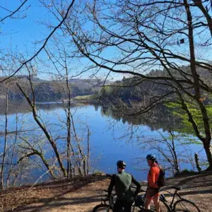 Twee fietsers kijken tussen kale bomen uit over een stil stuwmeer