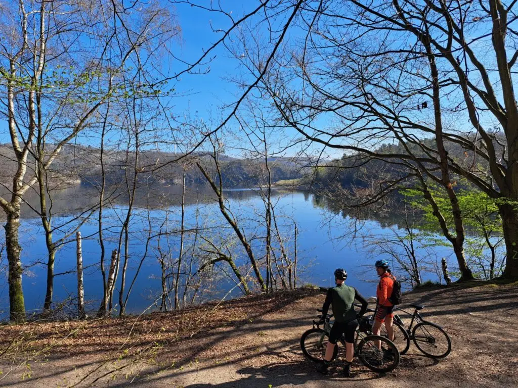 Twee fietsers kijken vanaf een bospad uit over een spiegelend stuwmeer